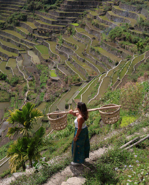 Portrait de Morgane portant un fléau avec deux paniers sur les épaules dans les rizières en terrasses de Banaue, site classé à l'UNESCO